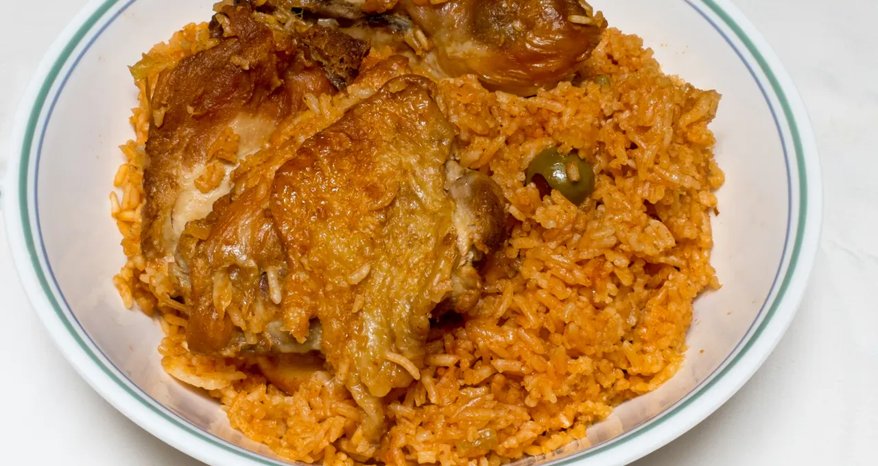 Locrio de pollo: orange rice, browned thighs and an olive, in a deep plate