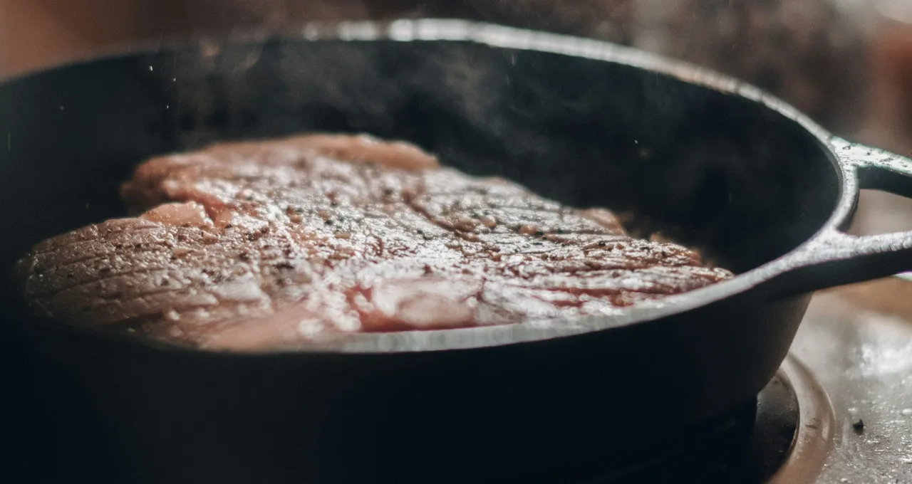 Thick steak searing in a black cast-iron skillet on an electric coil, steam rising