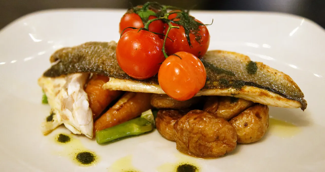 Pan-seared sea bass fillet with crispy skin, cherry tomatoes on the vine, and roasted potatoes