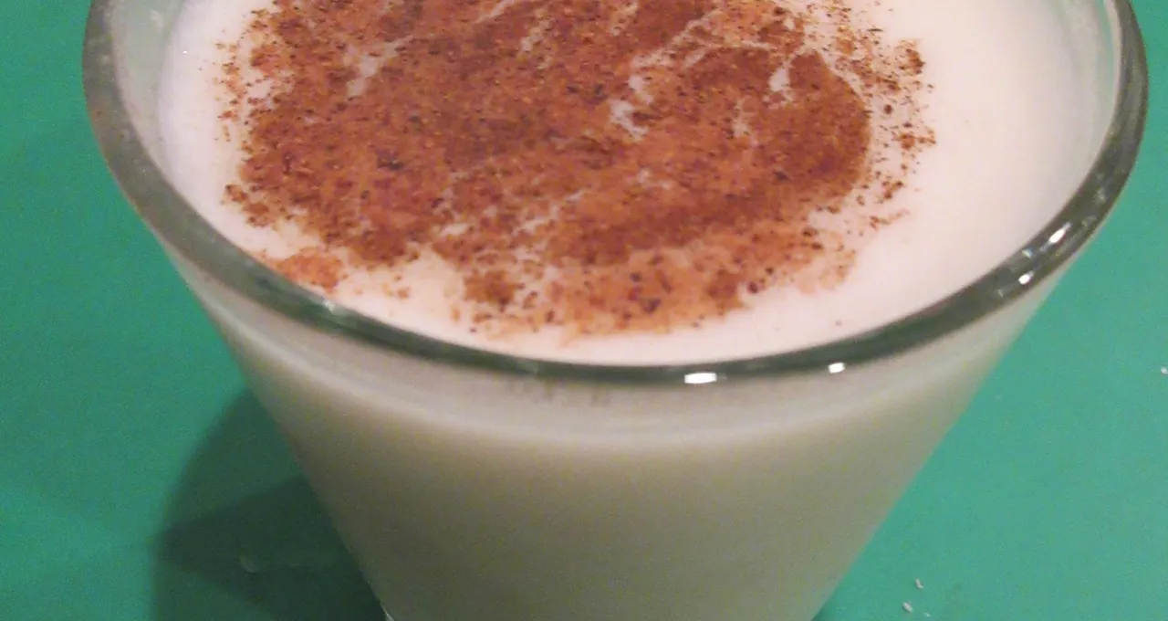 Close-up of a glass of coquito, ground cinnamon on the surface, on a green table