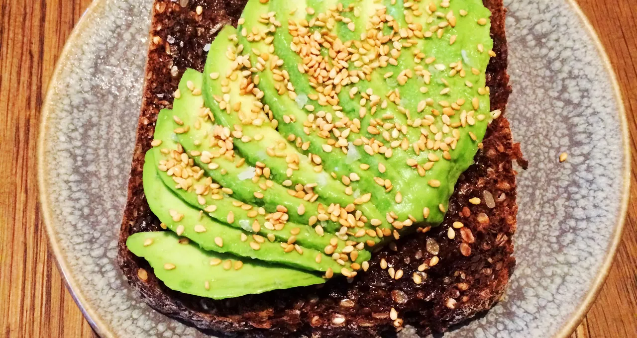 Sliced avocado on dark seeded toast, sesame seeds and salt, on a speckled plate