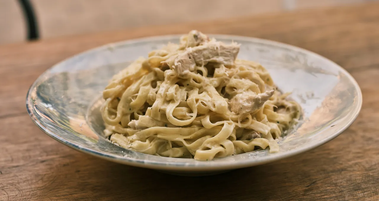 Creamy fettuccine with seared chicken and grated cheese in a shallow bowl on a wooden table