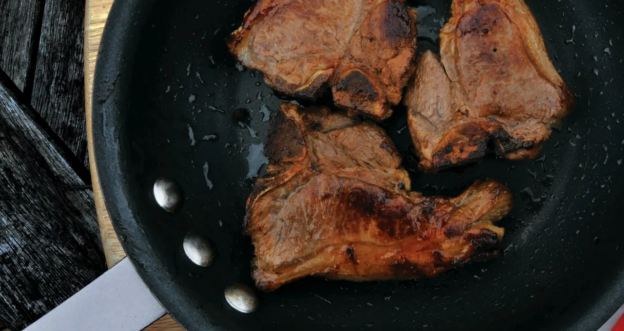 Three seared lamb loin chops in a black pan on a wooden board
