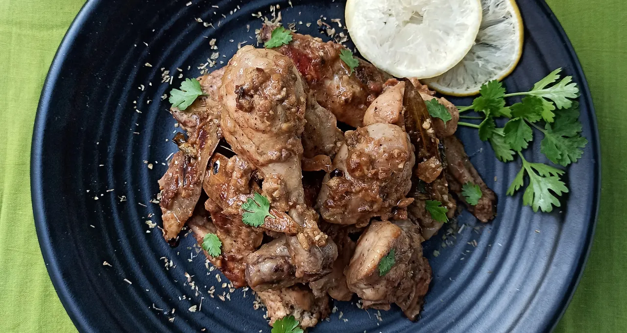 Bone-in lemon pepper chicken on a black plate, cilantro and lemon slices on top