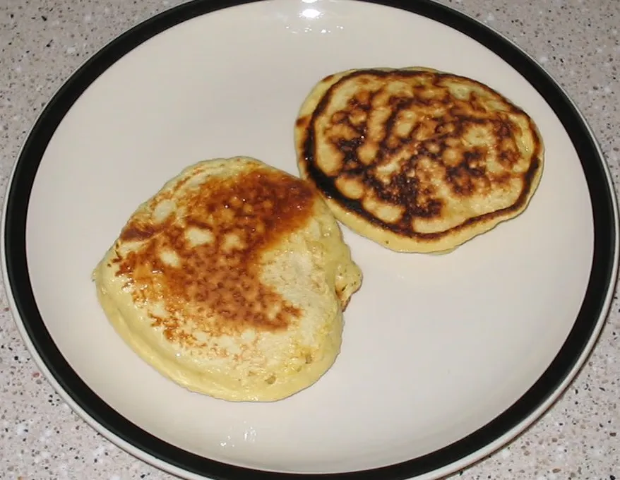 Two thick golden-brown pancakes on a large off-white plate with a dark rim