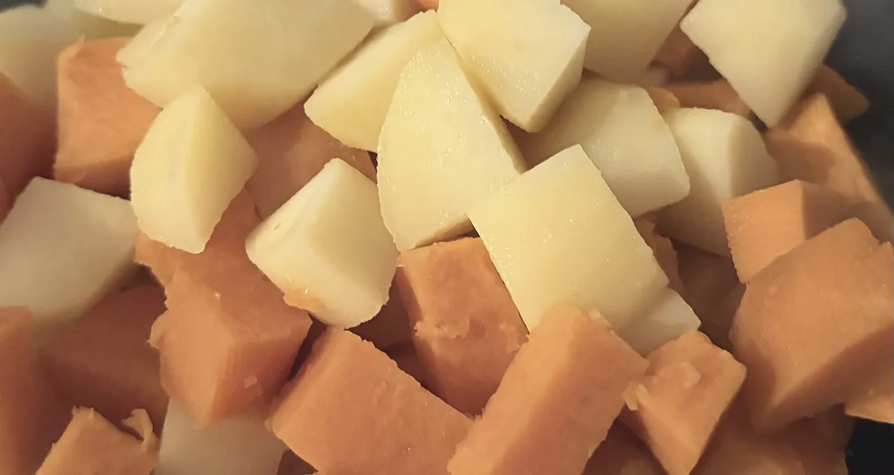 Parboiled cubes of pale potato and orange sweet potato piled together in a glass bowl