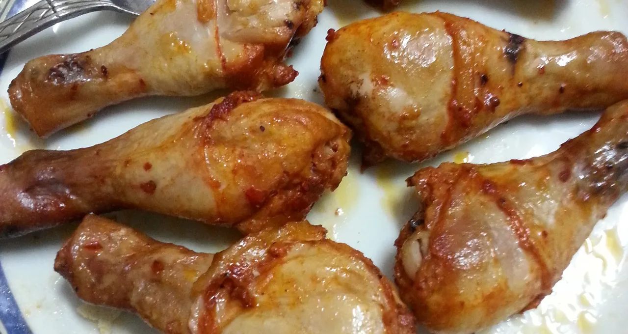 Six roasted chicken drumsticks on a white plate with a blue floral rim