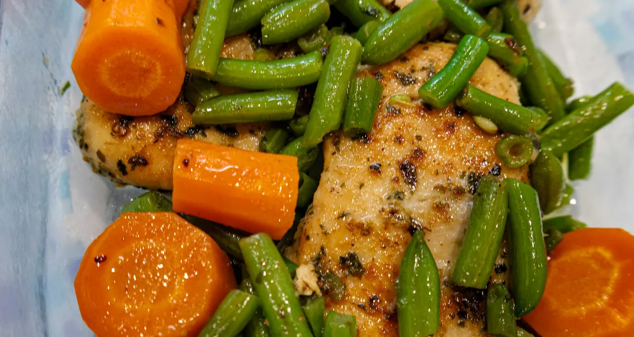 Two baked chicken breasts in a dish with green beans and thick carrot coins